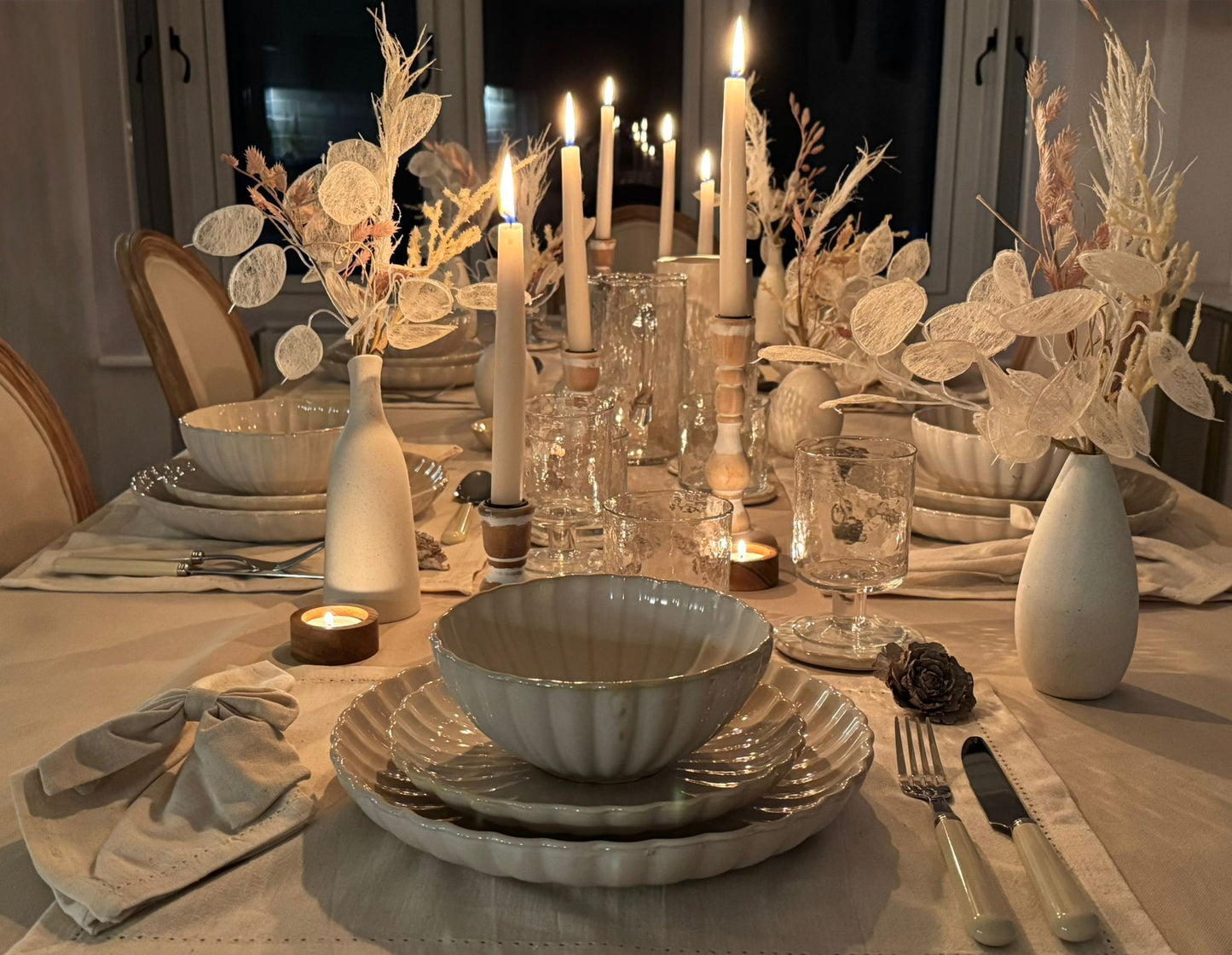Soft candlelight adding atmosphere to a minimalist, neutral-toned dining table setting for hire