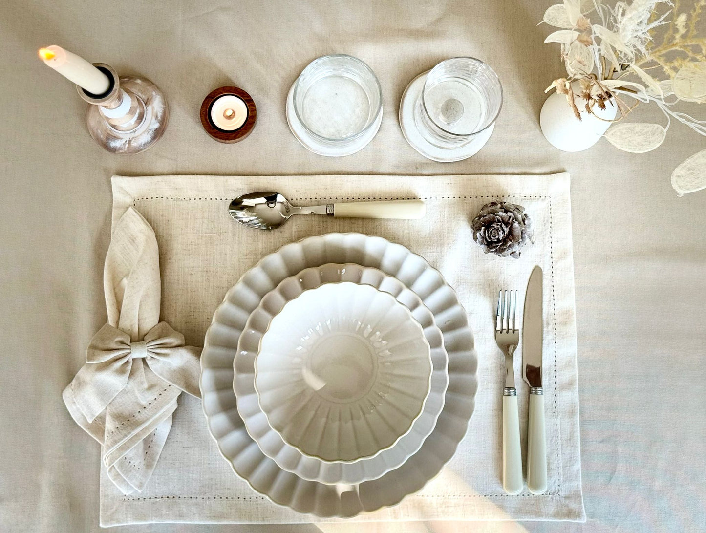 Clean, modern table setting featuring white ceramic plate, beige table , silver / white cutlery and decor elements for hire
