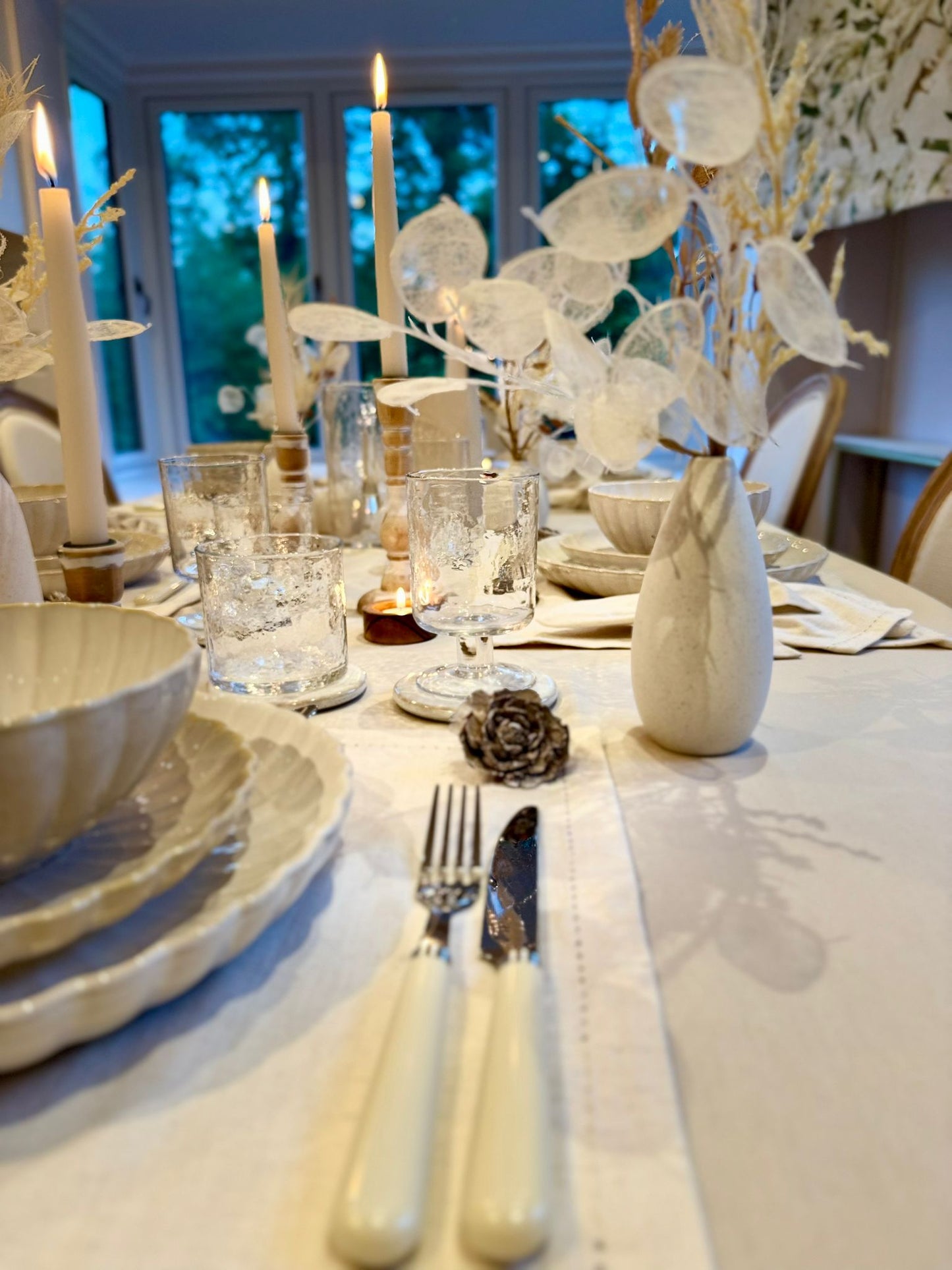 Clean, elegant table setting featuring white ceramic plate, beige table linens, and silver/white cutlery, glass wrae and decorative items for hire