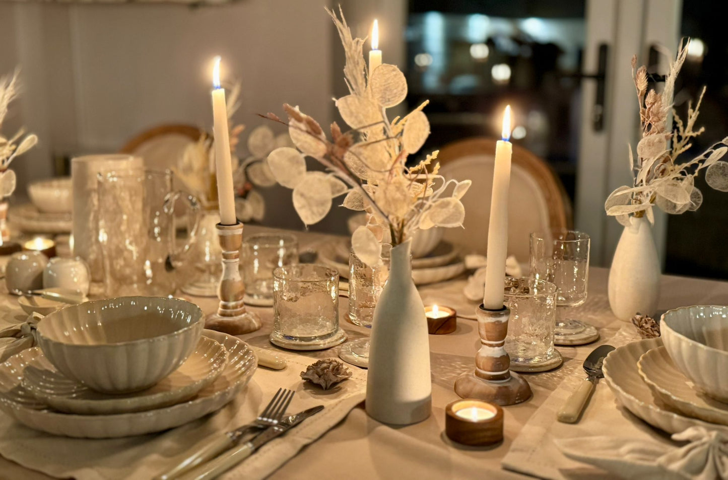 Soft candlelight adding atmosphere to a minimalist, neutral-toned dining table setting, highlighting bud vase, availablle for hire/rent