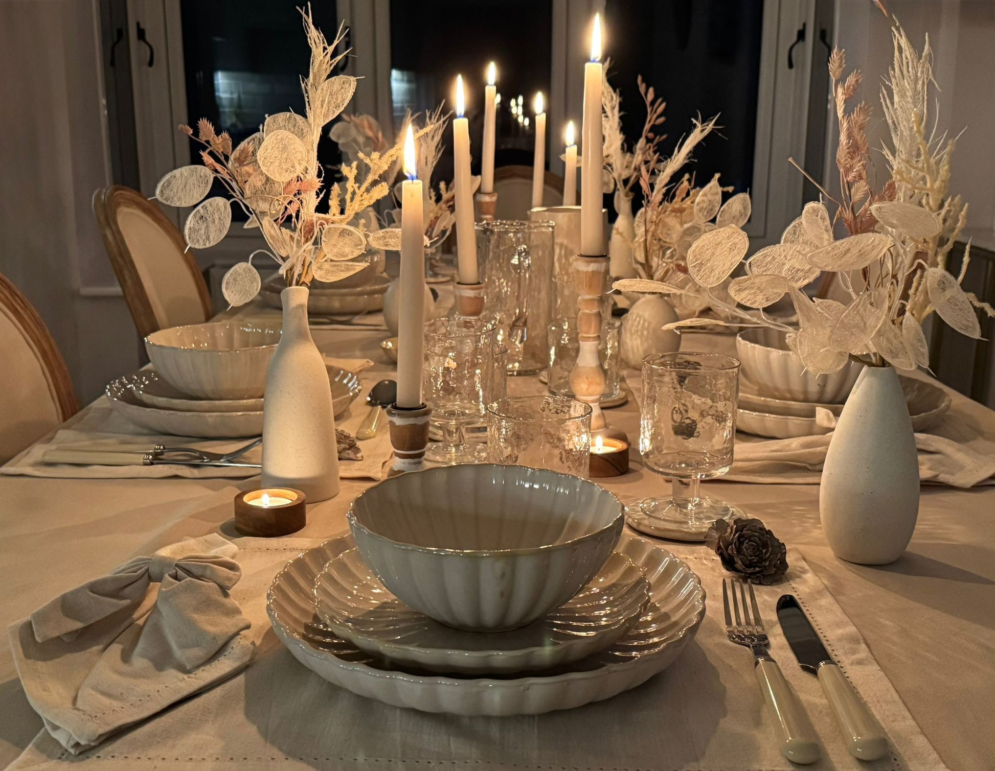 Soft candlelight adding atmosphere to a minimalist, neutral-toned dining table setting for hire