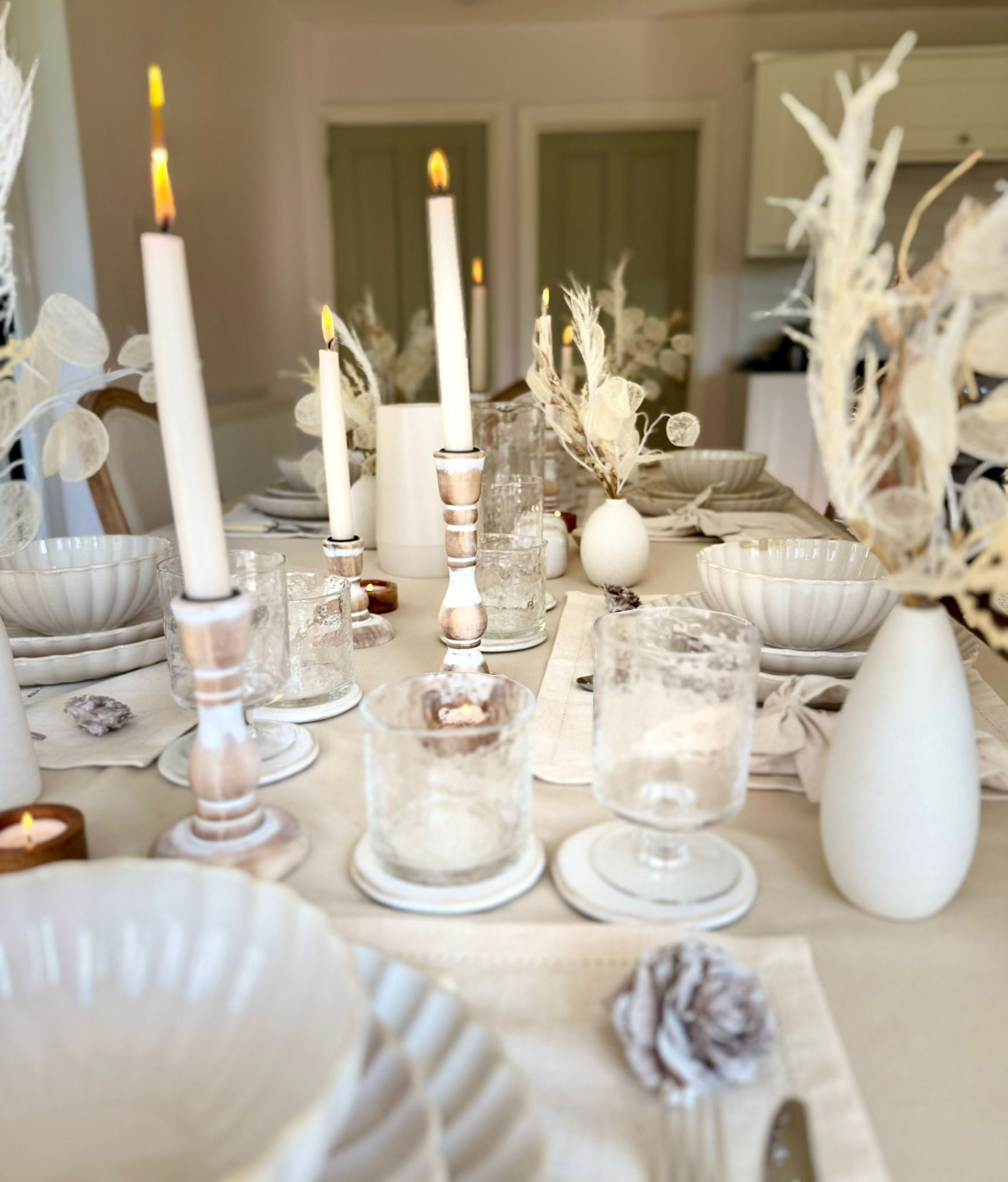 Clean, modern table setting featuring white ceramic plate,beige table linens, and  ceramic bud vases and wooden candlesticks